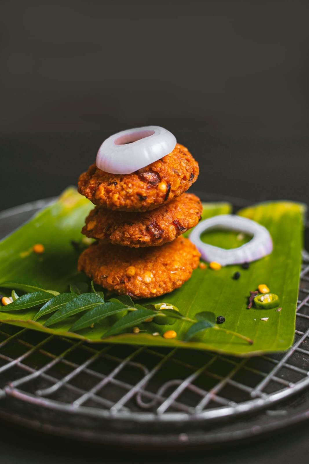 Stack of golden crispy vadas on banana leaf with onion ring garnishing