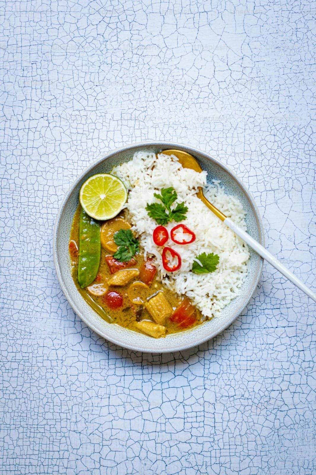 White bowl of yellow curry and steamed basmati rice with lime