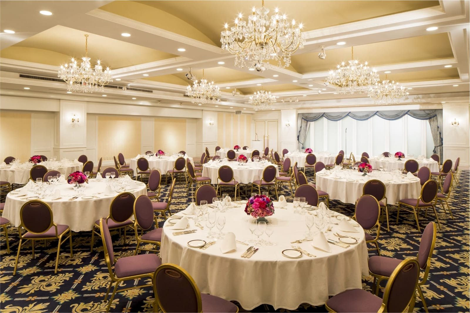 Luxury indoor wedding reception ballroom with round banquet tables and crystal chandeliers