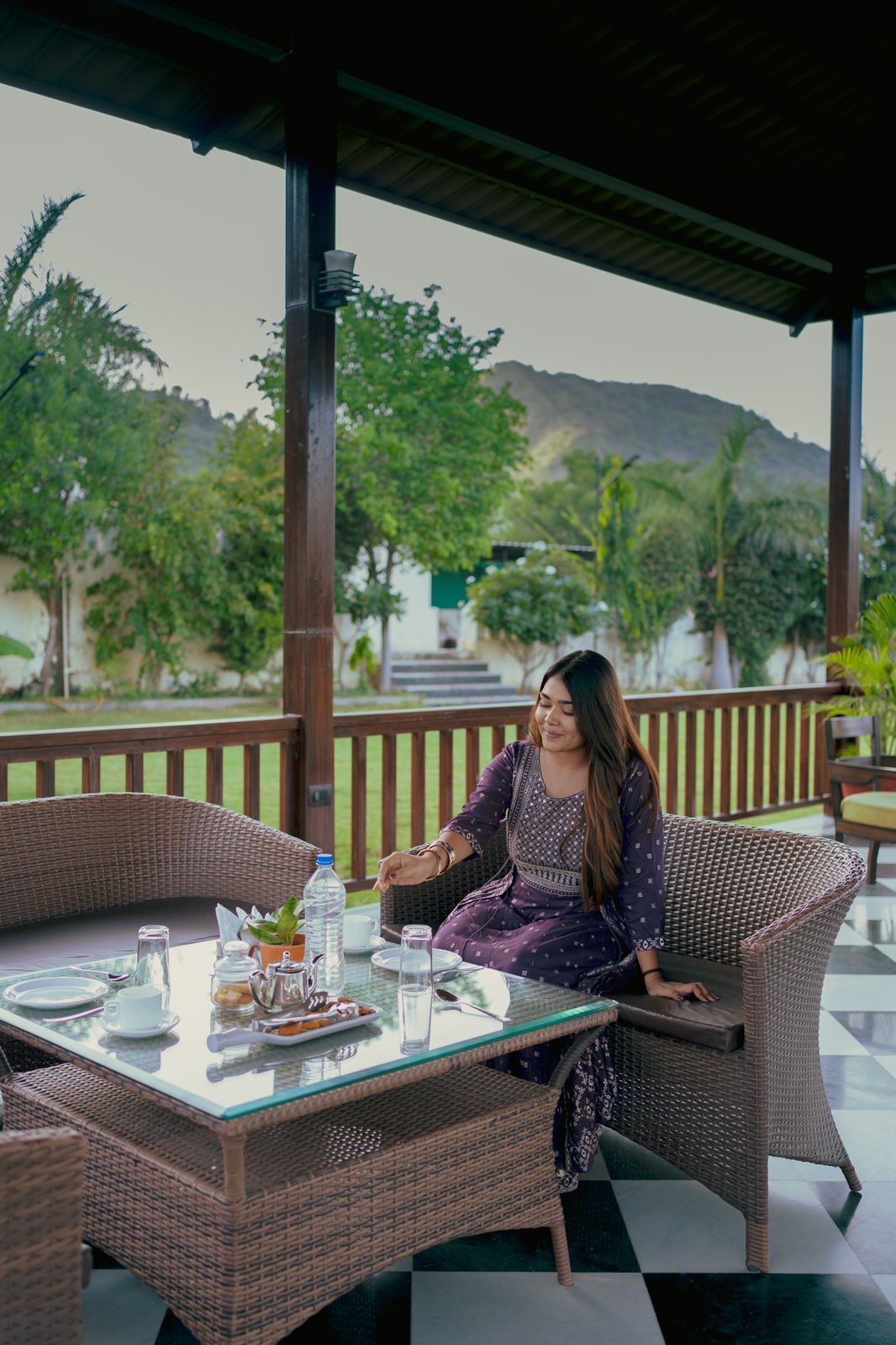 Woman seated at covered terrace dining table surrounded by greenery and scenic views in Udaipur